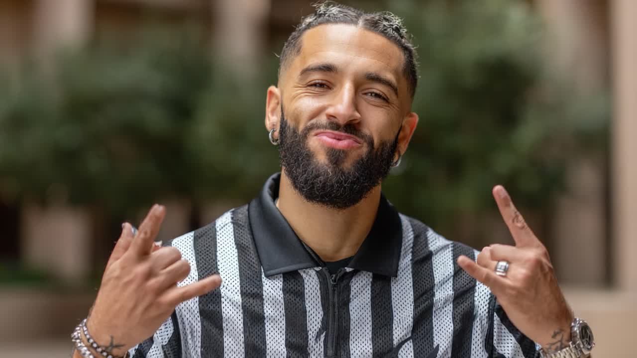 Smiling Individual in a Striped Shirt Poses with Hand Gestures in an Outdoor Setting, Exuding Confidence and Positivity in a Professional Environment