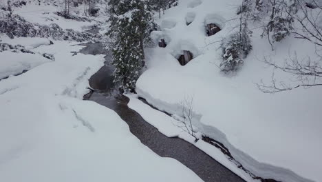 drone flying over a creek in a small snowy valley in the alps