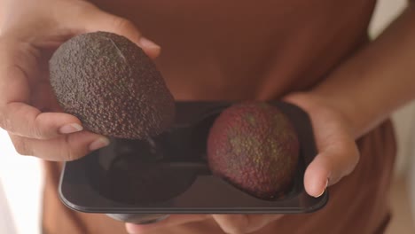 woman holding two avocados in a black container