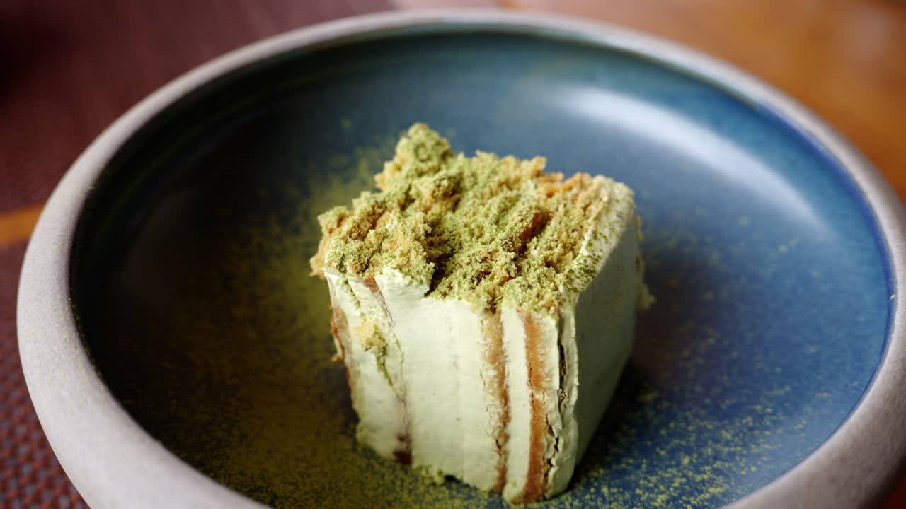 Close up of a piece of cake with matcha powder on a blue plate at a restaurant