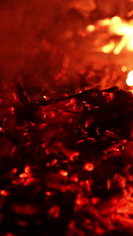 moving the glowing charcoal in the bonfire. beautiful flames and sparkles close up. vertical video