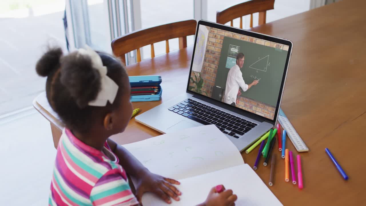 African american girl doing homework while having video call with male teacher on laptop at home