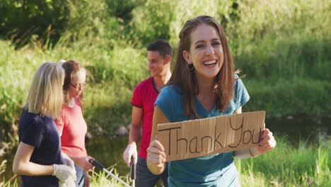 mid adult smiling and looking at camera with woman holding thank you sign during river clean-up day