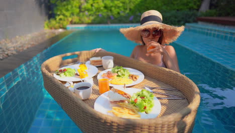 a young woman tourist has her own personal breakfast on a floating table in a private swimming pool