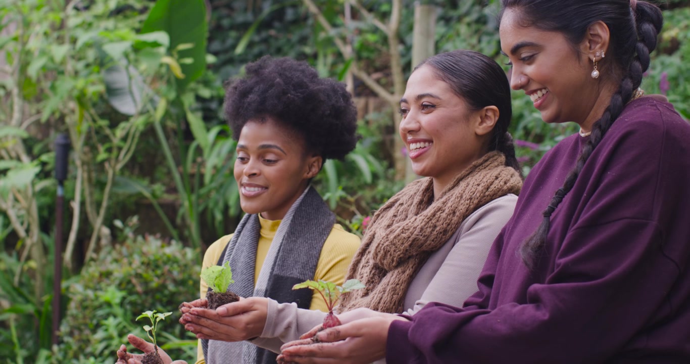 Amigas diversas no jardim trocando sorrisos, segurando mudas e apresentando plantas