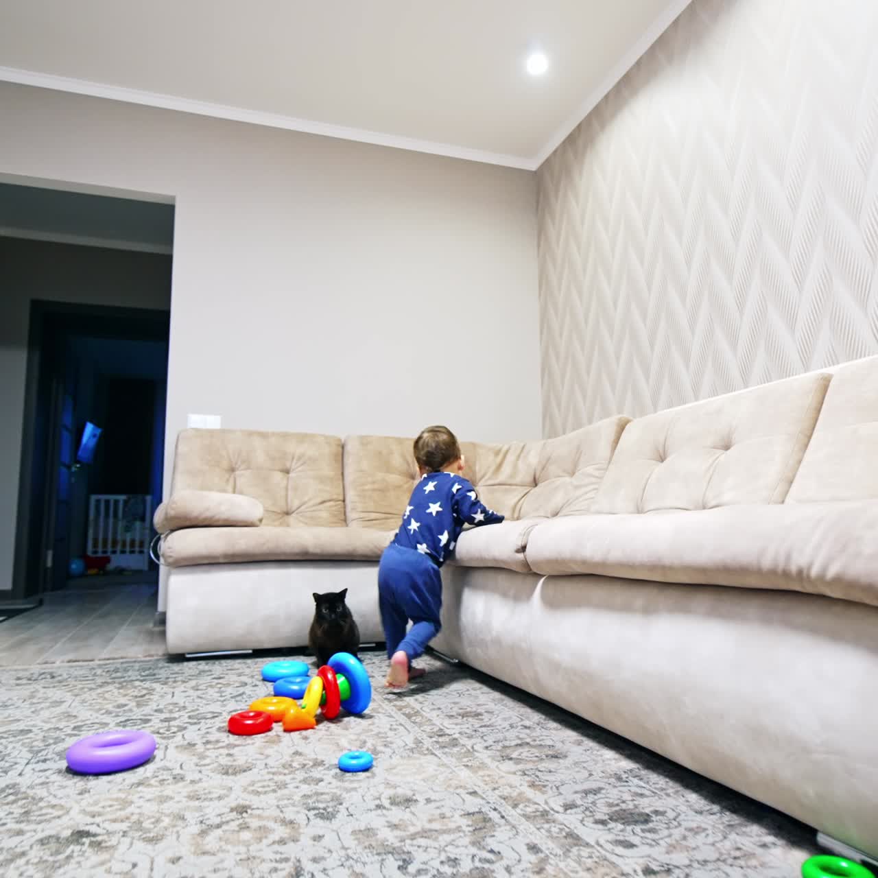 Happy laughing kid running by the room. Baby goes to the sofa stepping on the cat and scaring it off. Low angle view