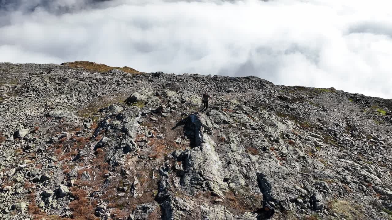 Drone ascends from man on Bakkanosi cliff, tilting down to reveal vast drop to Naeroyfjord and clouds below, creating illusion of standing on a floating mountain