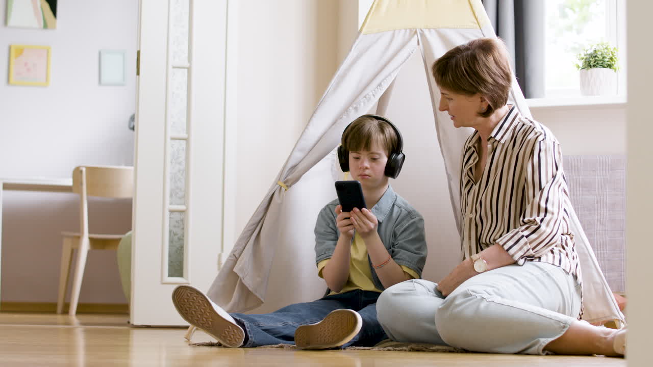 niña con auriculares usando un teléfono inteligente junto a su madre