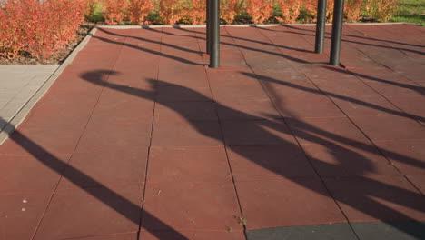 shadow of workout junkie performing side lunge exercise on outdoor gym court under afternoon sun, long shadows stretching across textured rubber tiles framed by autumn shrubs and metal bars