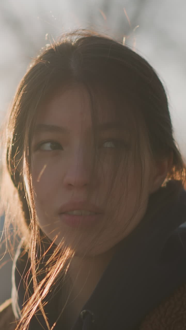 close-up shot of a girl walking with her hair partially covering her face, expressing a profound sense of grief. The soft backlighting from the sunset enhances the somber mood