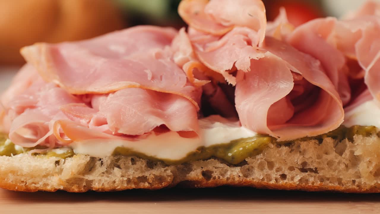 Mortadella ham sandwich, Traditional italian focaccia filled with thin pesto slices of mortadella, served by chef man in cafe restaurant. Macro of traditional italian spanish tapas antipasti.