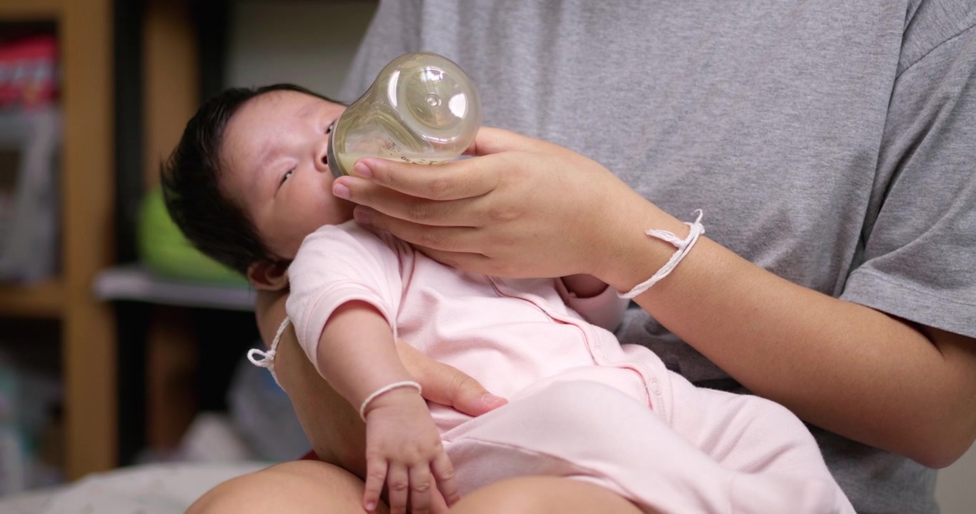 Una neonata sdraiata in grembo alla madre sta bevendo del latte da un biberon tenuto dalla madre.