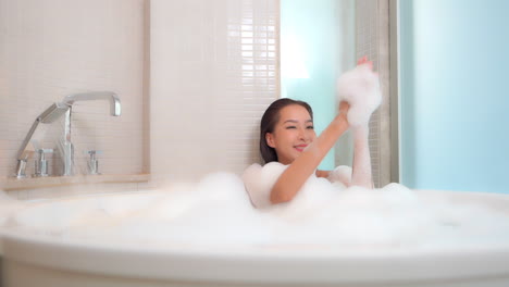 woman taking a hot bath relaxing in a bathtub filled with foam inside a hotel room