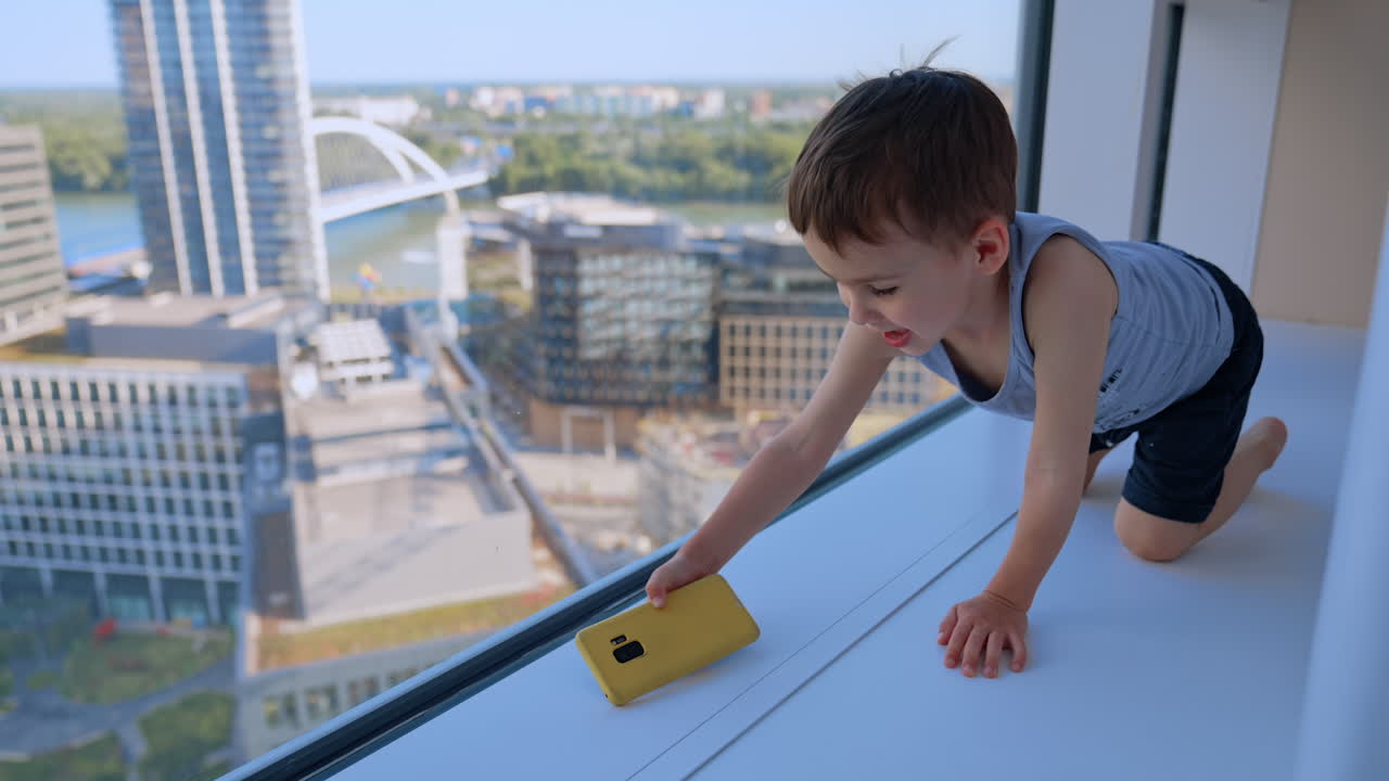 Boy by high-rise window. A cheerful young boy leans on a window ledge in a modern building, enjoying the city view from above