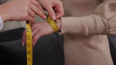 close-up of a tailor measuring a young woman's hand before sewing a dress.