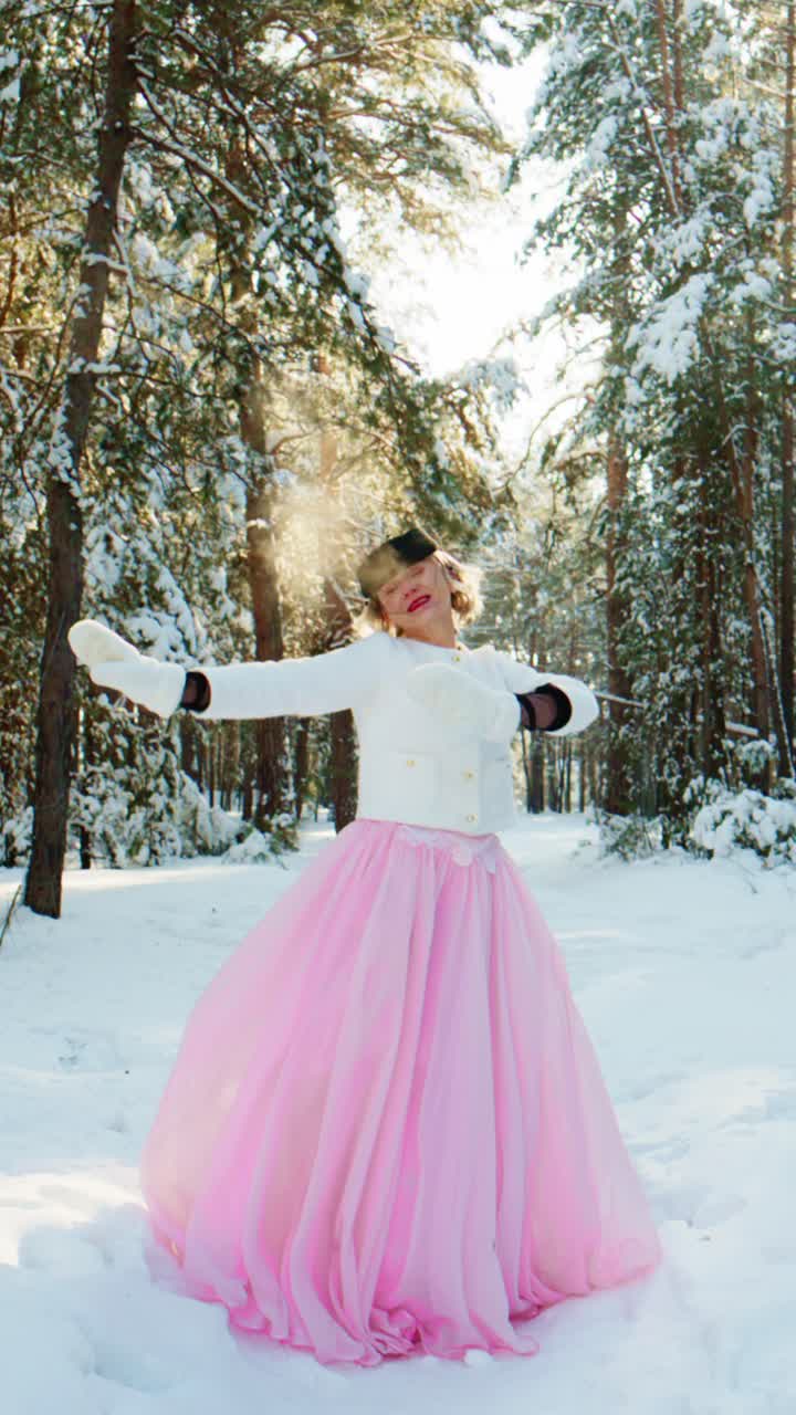Donna gioiosa con gonna rosa che raccoglie la neve in una foresta invernale.