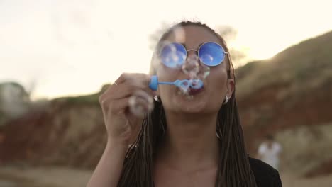 young female hipster with dreads cheerfully making soap bubbles on the beach in the evening. slow motion shot