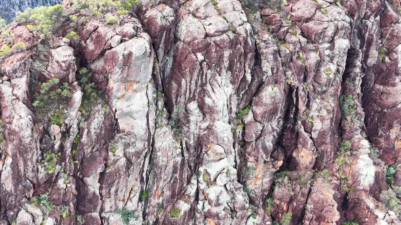 Drone glides over rugged volcanic sandstone cliffs, revealing bushland below in soft morning light