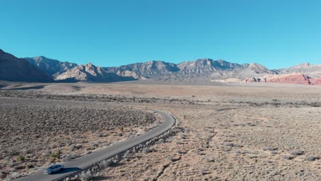 Aerial-drone-shot-of-Red-Rock-Scenic-Highway-with-mountains-in-the-background