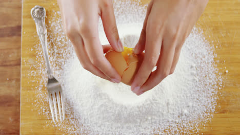 woman breaking eggs in the flour on wooden board 4k