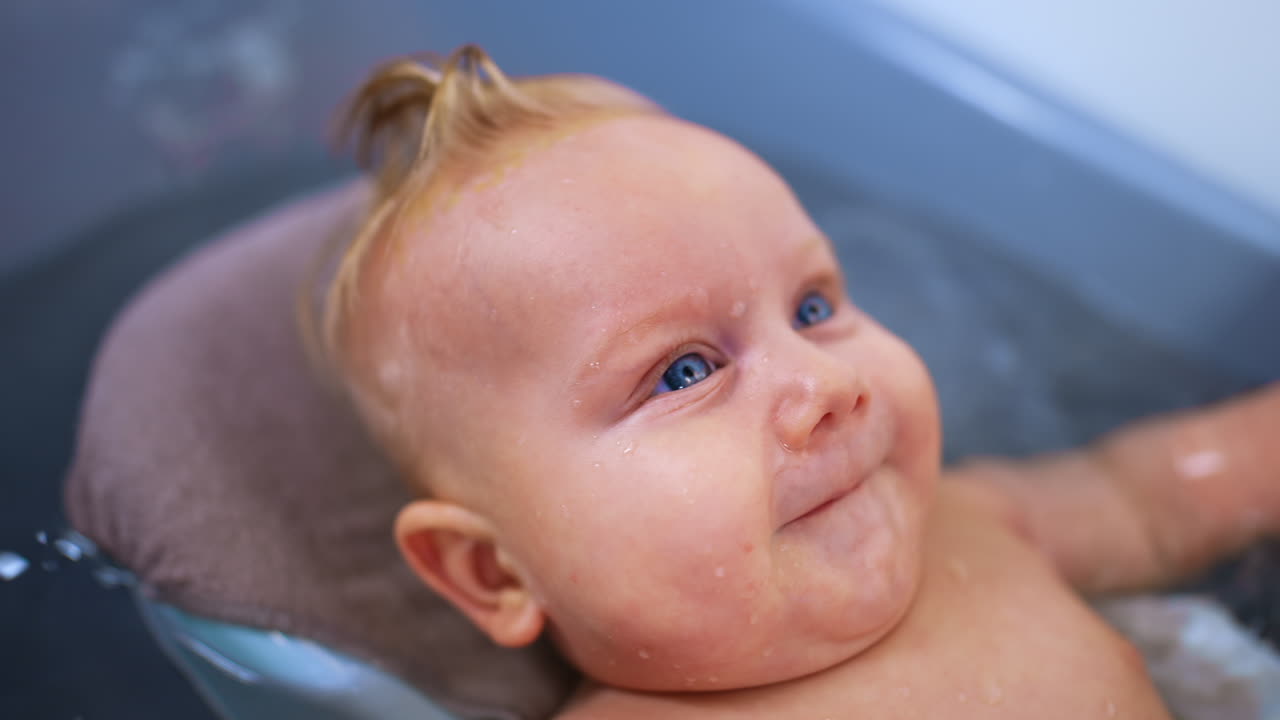 Beautiful face of a Caucasian baby with big blue eyes. Close up. Little child lies in a bath.