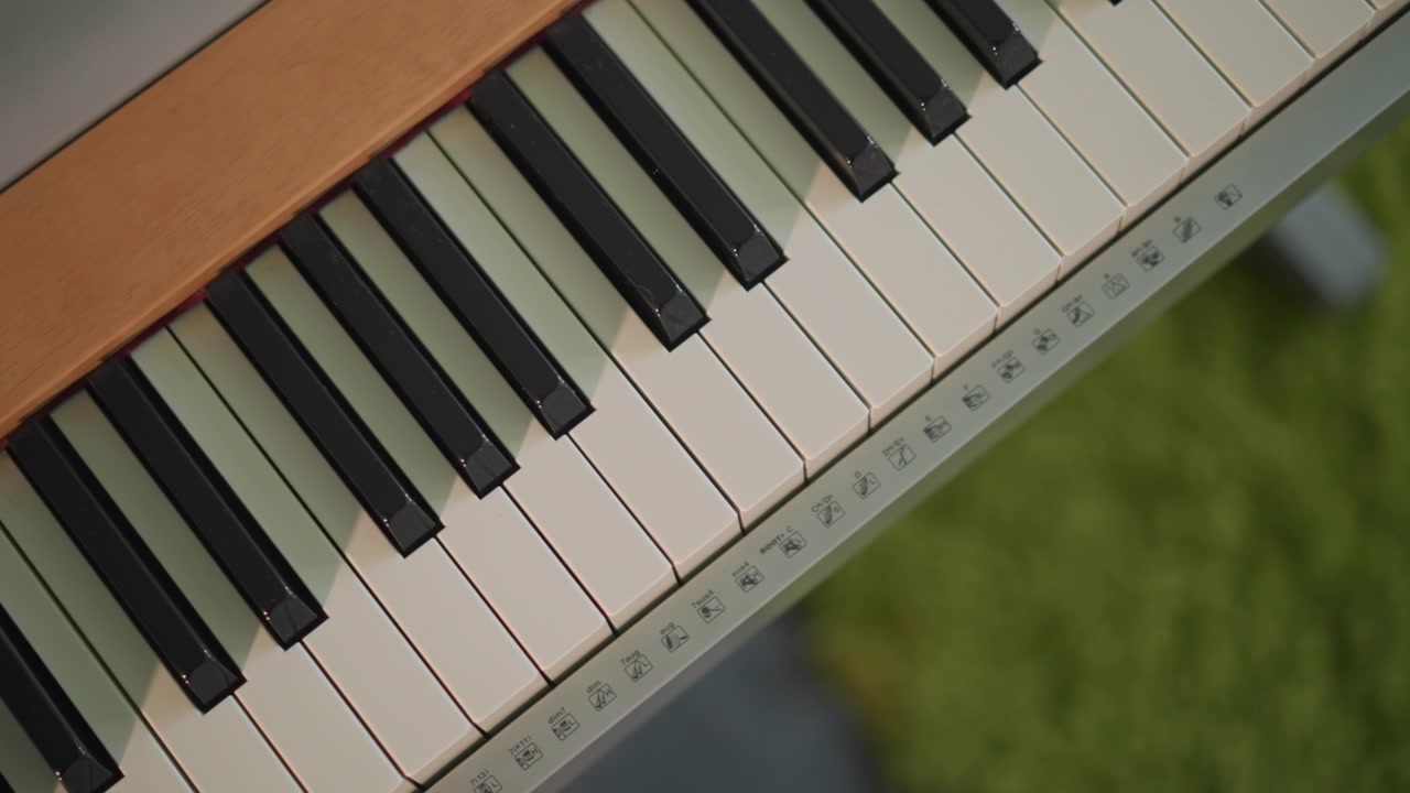 Nærbillede af keyboard ovenfra, der viser pianotangenter i et klasseværelsesmiljø. Et vintage elektrisk keyboard står på et stativ over et grønt tæppe, med fokus på de elfenbensfarvede og sorte tangenter, diskrete slidmærker og fingerplacering.