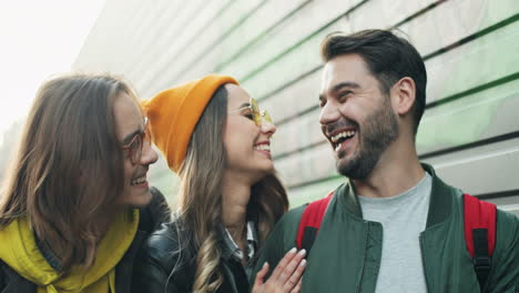 close-up view of young handsome caucasian man using smartphone in the street, then his cheerful friends comming up and they hugging and laughing