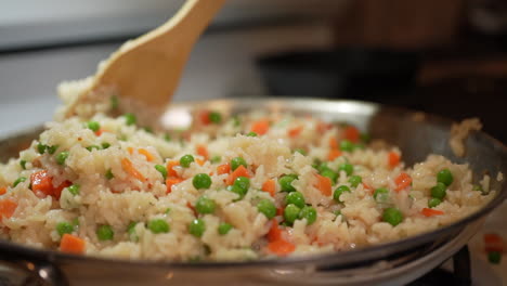 stirring fried rice as it cooks on the wok with peas and carrots - slow motion