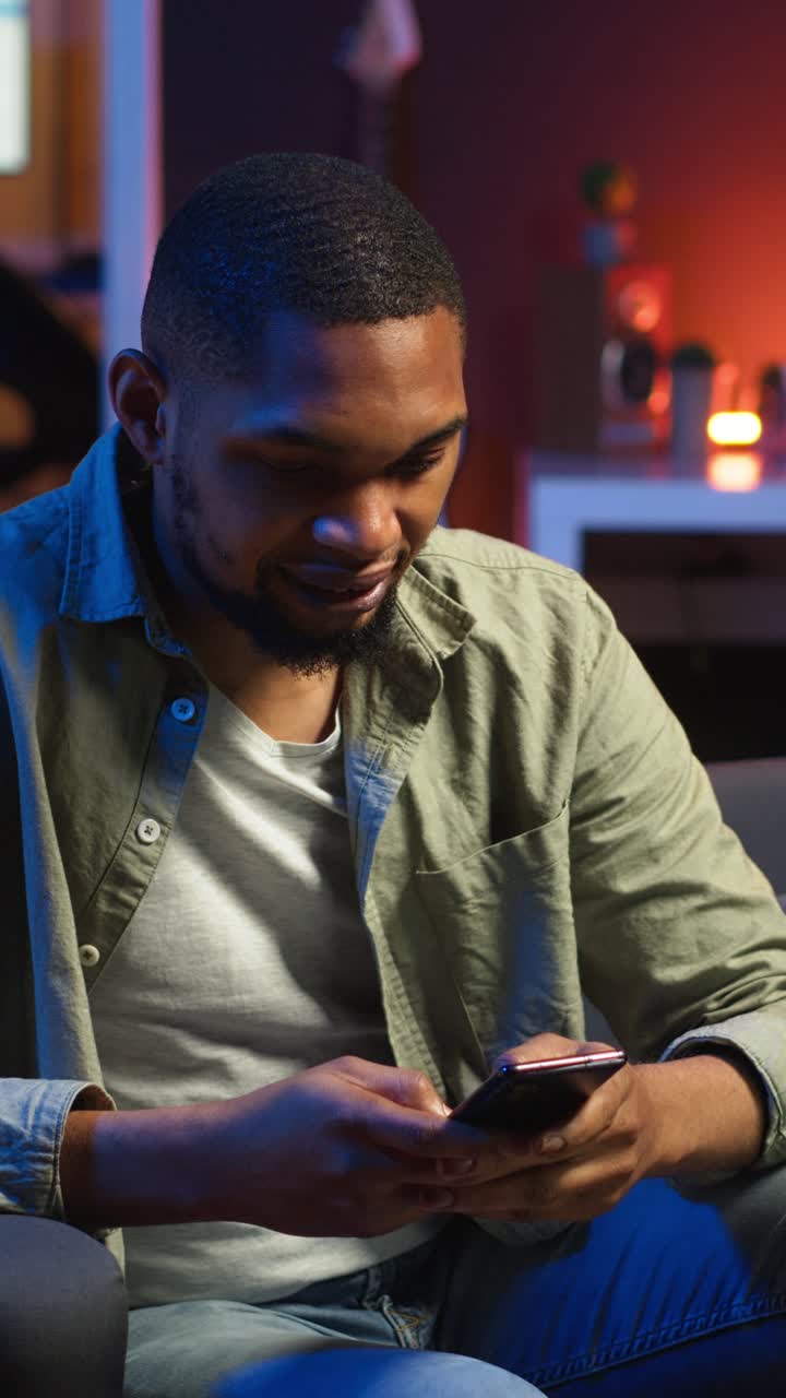 Vertical Video African american person texting messages on a smartphone app on the sofa