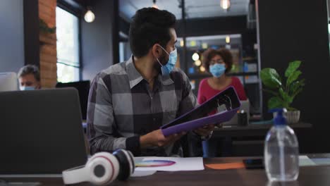 Middle-eastern-man-wearing-face-mask-giving-file-of-documents-to-his-female-colleague-at-modern-offi