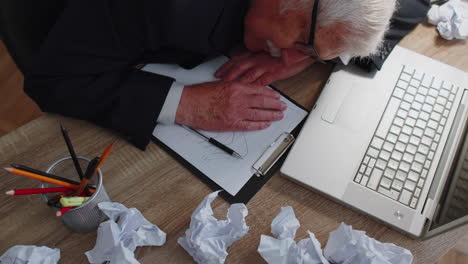 cansado, somnoliento, sobrecargado de trabajo, anciano, hombre de negocios, se queda dormido, se sienta en su escritorio de la oficina con una computadora portátil.