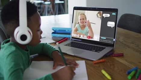 escolar que usa una computadora portátil para una lección en línea en casa, con un amigo de la escuela y un chat web en la pantalla