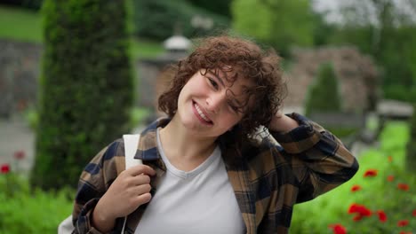 Portrait-of-a-happy-brunette-girl-in-a-plaid-shirt-with-a-backpack-walking-in-the-park-while-studying-at-the-university