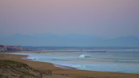 panorámica cinematográfica de cerca hacia biarritz peir impresionante ver temprano en la mañana enormes olas se hinchan surf hossegor seignosse francia rosa púrpura crepúsculo amanecer en la playa paisaje de la costa de la montaña