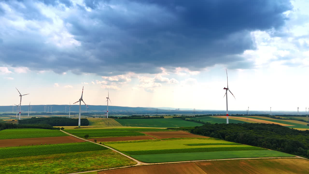 Turbines generate energy in fields. Wind turbines rotate steadily in expansive green fields under a dramatic sky, showcasing renewable energy in action