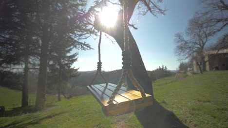 Primer-Plano-De-Un-Columpio-Colgado-De-Un-árbol-Que-Se-Mueve-Con-El-Viento-Bajo-El-Sol-En-El-Campo-En-Un-Jardín-En-Francia,-Ardèche