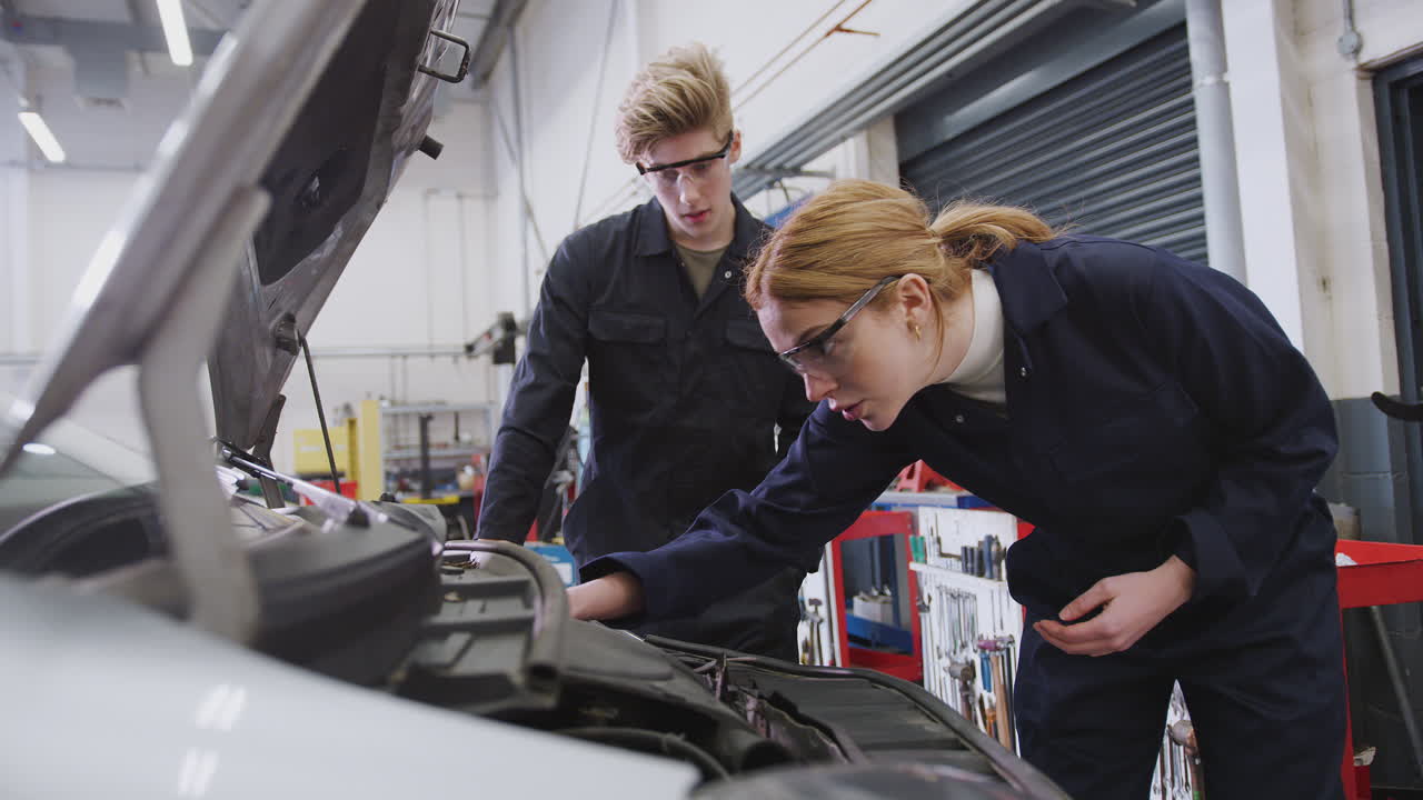 estudiantes masculinos y femeninos mirando el motor del coche en el curso de aprendizaje de mecánico de automóviles en la universidad