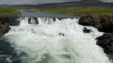 a river in iceland flowing strongly over rocks with hills and clouds in the background