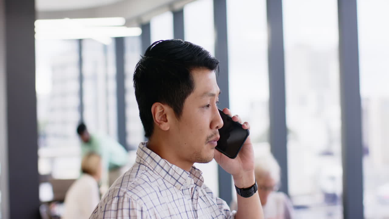 Talking on smartphone, man in office setting focusing on conversation