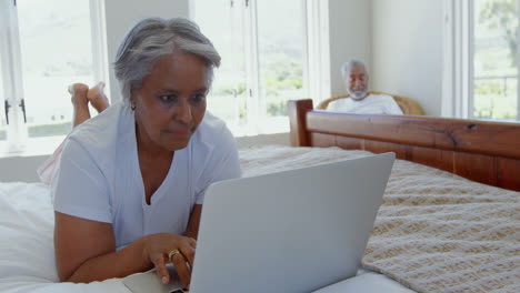 front view of senior black woman lying on bed and using laptop in bedroom of comfortable home 4k