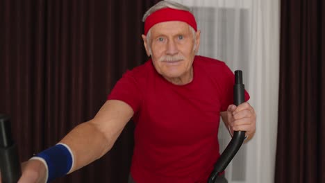 healthy elderly senior grandfather model exercising sport workout on orbitrek in room at home