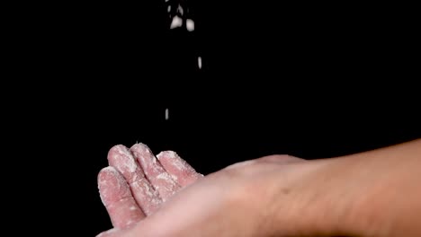 An-athlete-preparing-for-workout-by-rubbing-and-chalking-his-hands-with-the-chalk-powder,-isolated-on-black-background