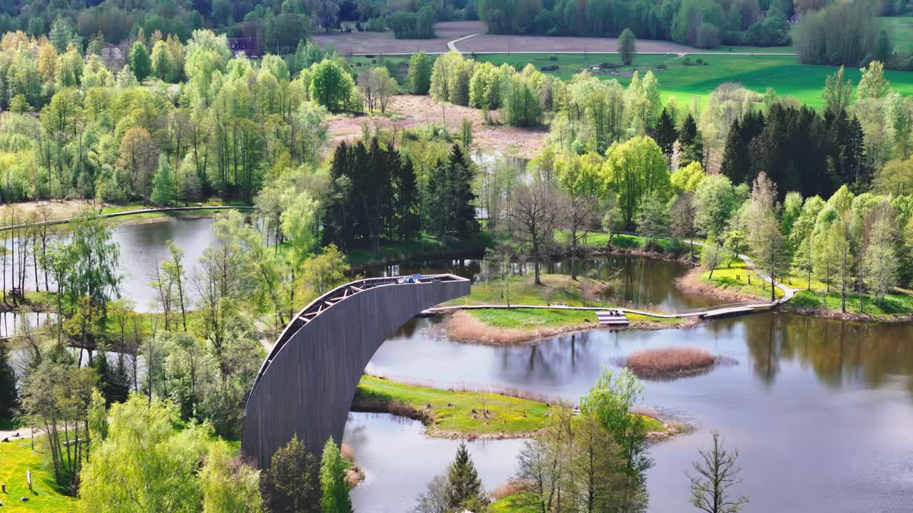 A Picturesque View From the Kirkilai Observation Tower Unveils Winding Boardwalks, Tranquil Karst Lakes, and Lush Forests in Biržai Regional Park, Lithuania - Aerial Pullback Shot