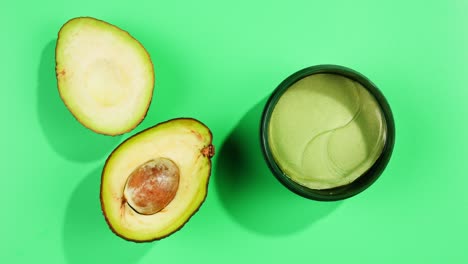 fresh ripe avocados with cream and essential oil on green background with mint mentol, make up cosmetics