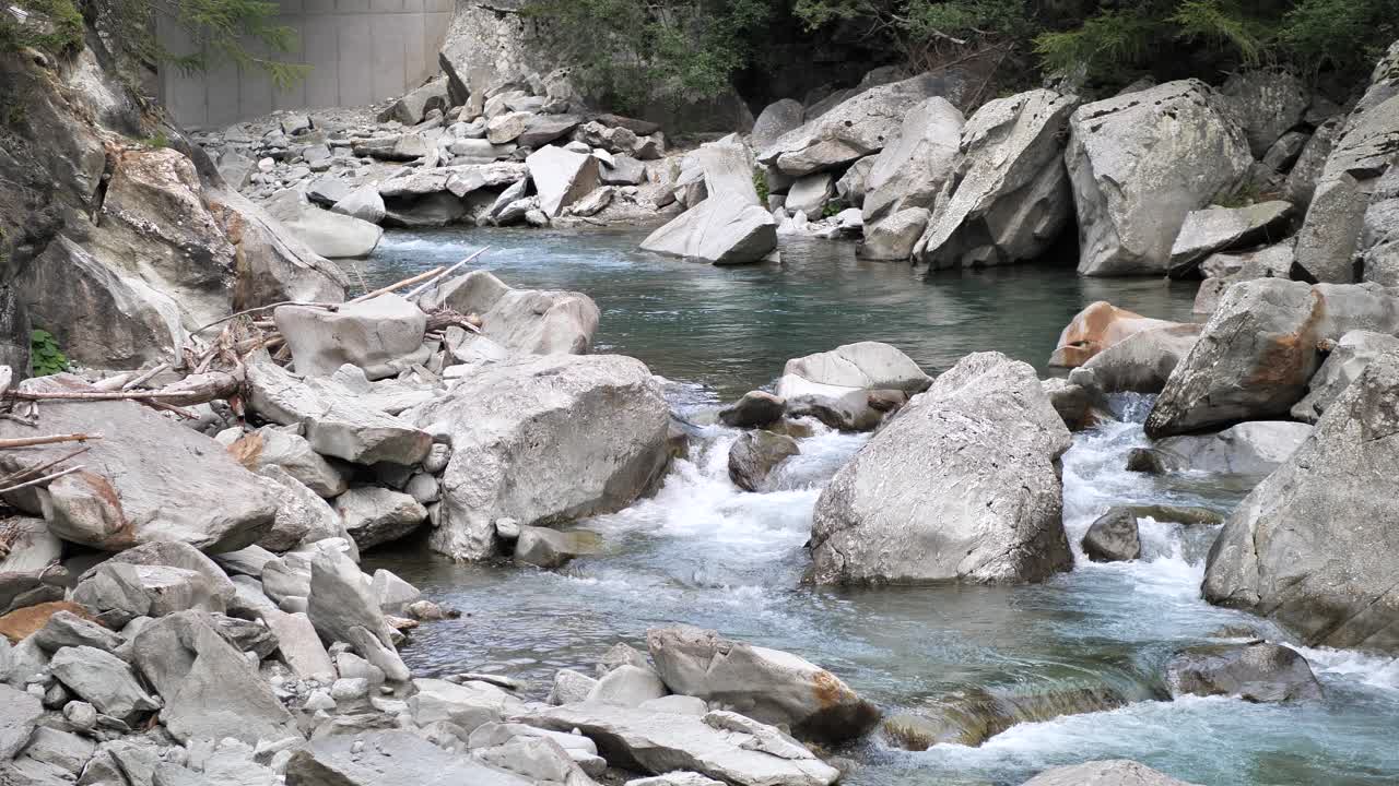 Clear blue melted water streaming true the rocks and green trees on the side and falling down on a small waterfall in Lauterbrunnen Switserland. Wide shot