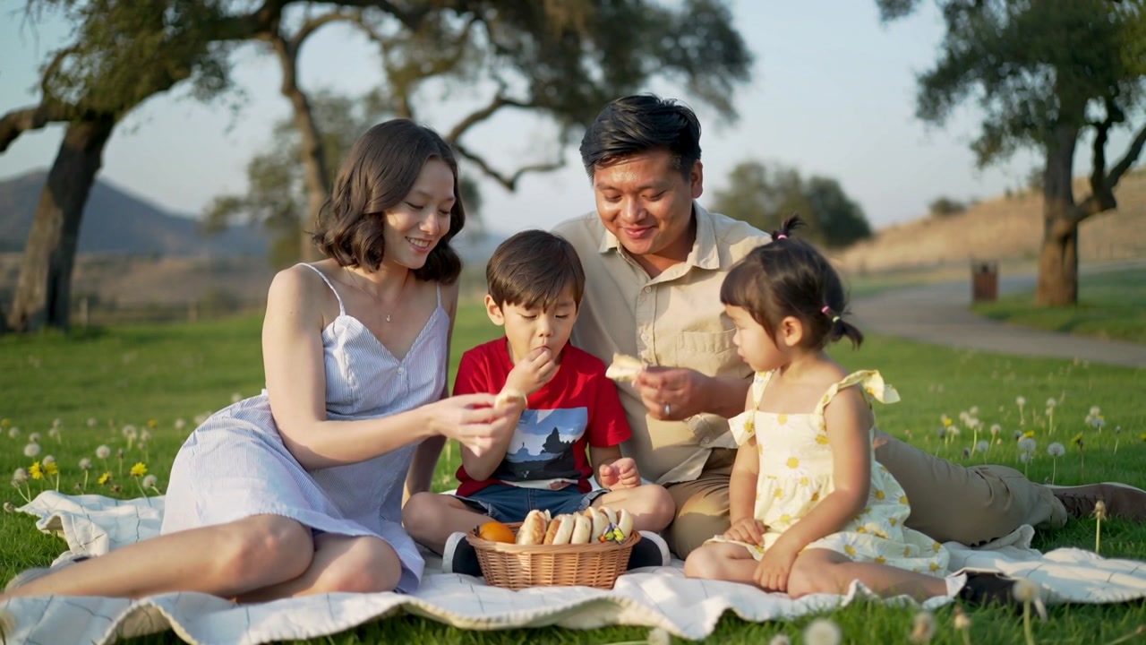 Reaching parents in summer clothes offering rolls to children at park, sharing with woven basket