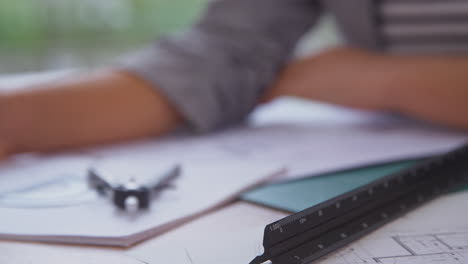 Close-Up-Of-Female-Architect-In-Office-At-Desk-Working-On-Plans-For-New-Building