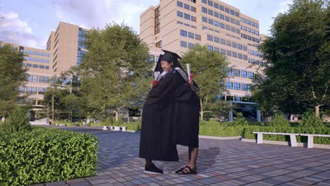 full body of asian woman students graduate in caps and gowns with diplomas smiling and hugging each other in front of a magnificent university building