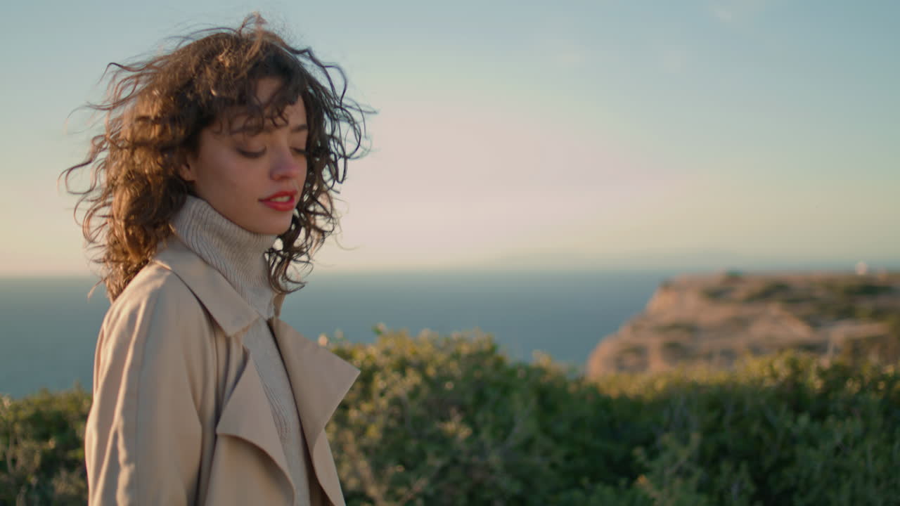 Donna casual che si dirige verso l'oceano e la montagna di sera. Ragazza serena che guarda la fotocamera e si gode il momento.