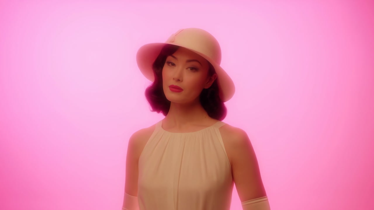 Woman In Pink Studio Wearing Hat Poses As Retro Fashion Model With Soft Cinematic Glow, Cream Dress